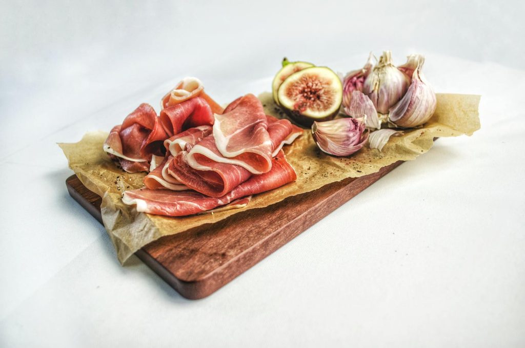 Elegant display of prosciutto, fresh figs, and garlic on a wooden board for culinary enthusiasts.