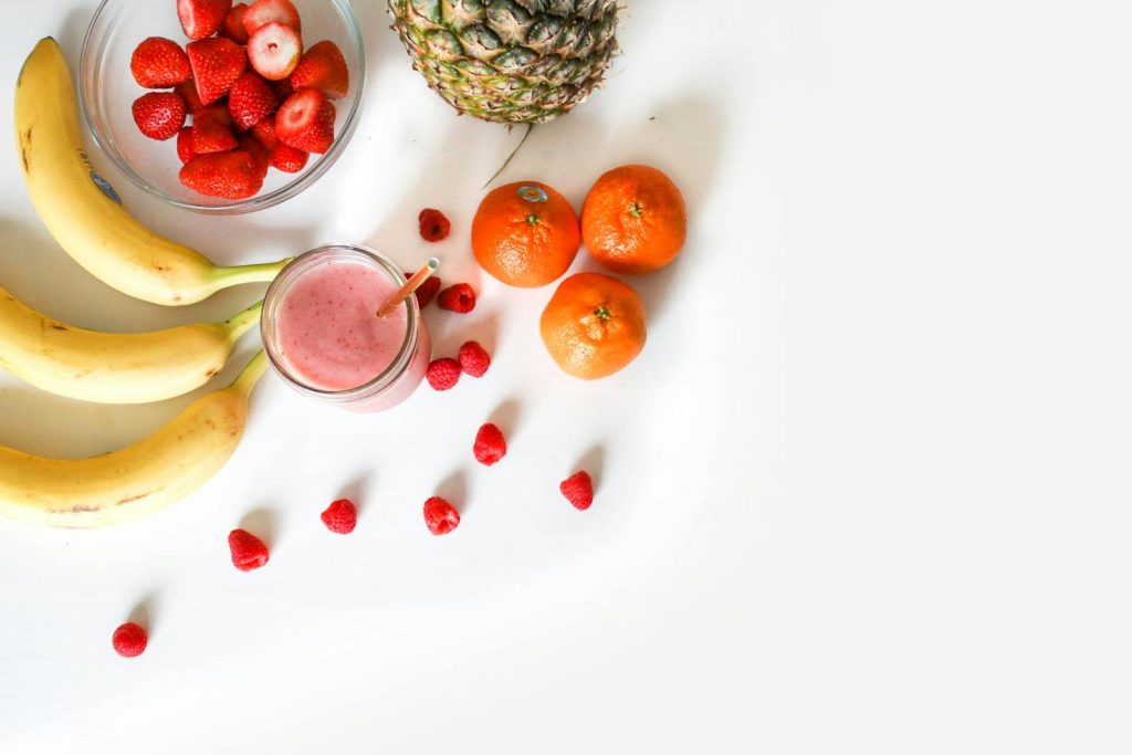 A vibrant flat lay of tropical fruits including bananas, strawberries, and a smoothie on a white background.